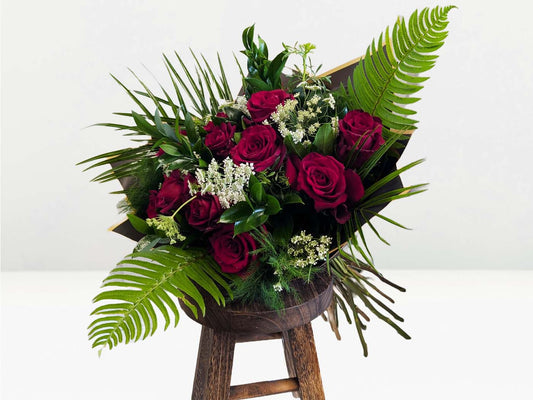 Bouquet of red roses and greenery on a wooden stool against a white background